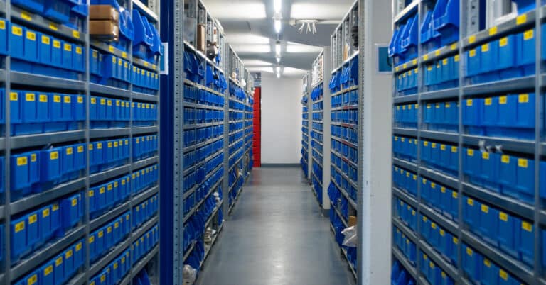 Small, blue replacement parts storage racks in a manufacturing warehouse.