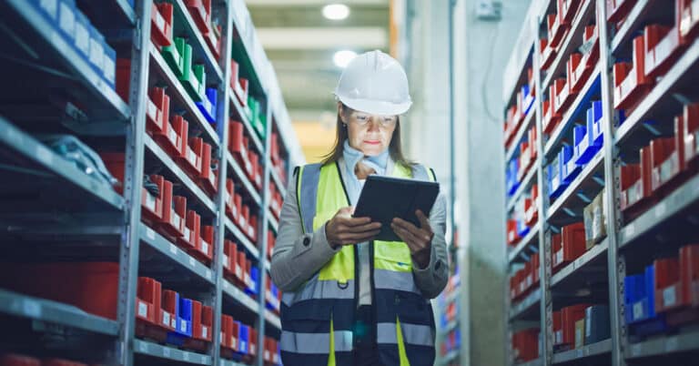 Manager with tablet PC checking inventory in manufacturing storeroom.