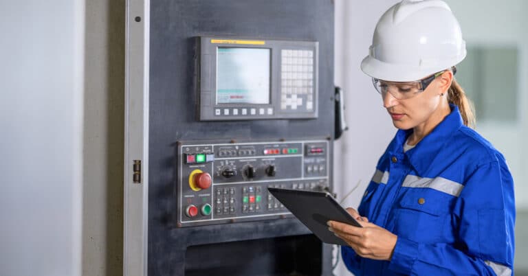 Female engineer standing in front of a CNC machine and reading the results in a tablet in factory.